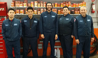 Five mechanics in blue uniforms standing in the Art's Automotive shop bay